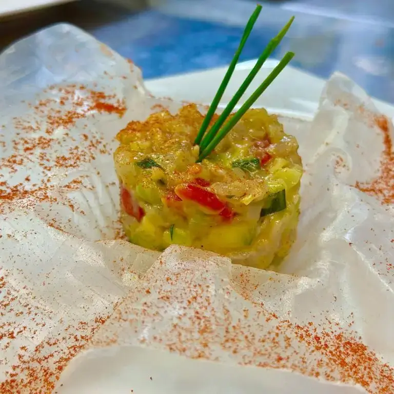 A small round vegetable tartare with chives plated on translucent paper at Rigatoni Ibiza.