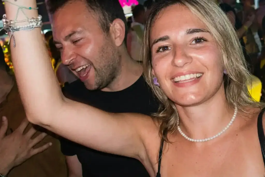 Smiling woman raising her arm and a man laughing beside her at a lively Rigatoni Ibiza event.