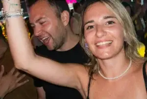 Smiling woman raising her arm and a man laughing beside her at a lively Rigatoni Ibiza event.