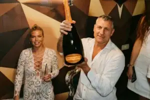 A man holds a Bellavista champagne bottle and a woman smiles beside him at a Rigatoni Ibiza party.