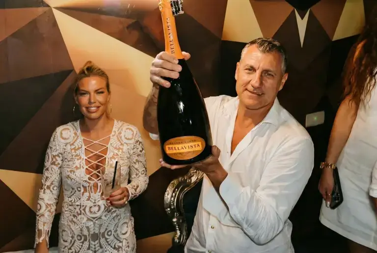 A man holds a Bellavista champagne bottle and a woman smiles beside him at a Rigatoni Ibiza party.
