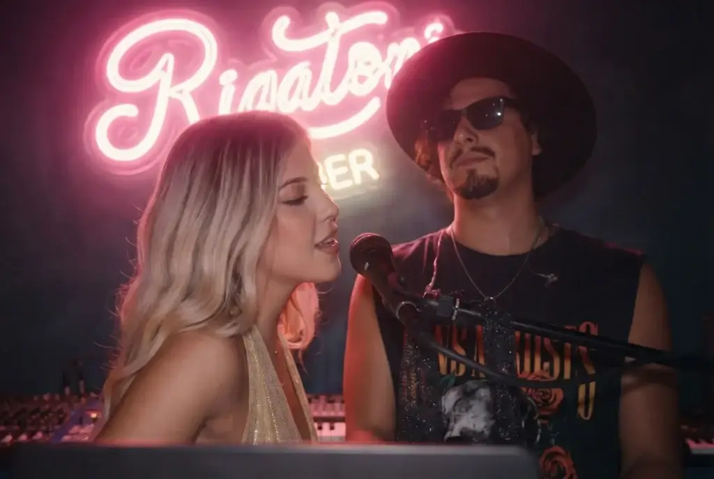 A woman sings into a microphone beside a man in sunglasses under a neon Rigatoni sign in Ibiza.