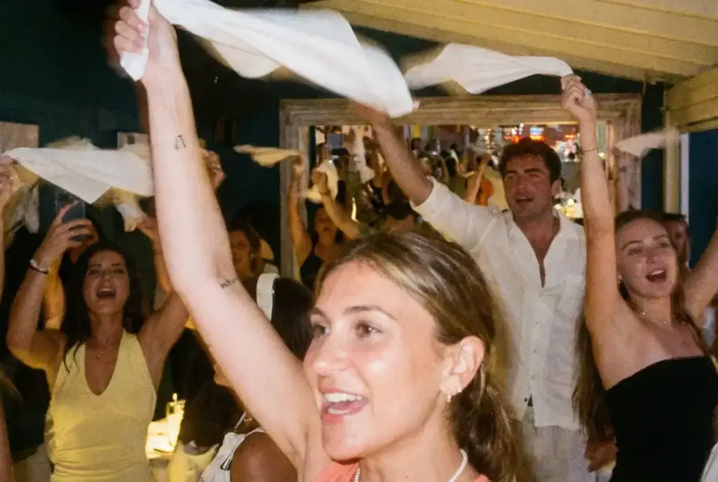 A group of people joyfully waving white napkins in the air during a lively Rigatoni Ibiza celebration.