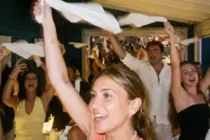 A group of people joyfully waving white napkins in the air during a lively Rigatoni Ibiza celebration.