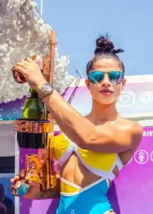 Woman in a colorful swimsuit and sunglasses holds a champagne gun at a boat party in Ibiza.