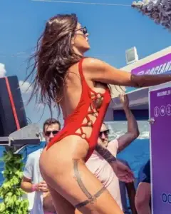 Woman in a red swimsuit dancing at an Ibiza boat party near the ocean with people and blue sky.